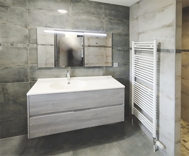 Salle de bains, carrelage aspect pierre, meuble vasque et sèche serviettes à eau.